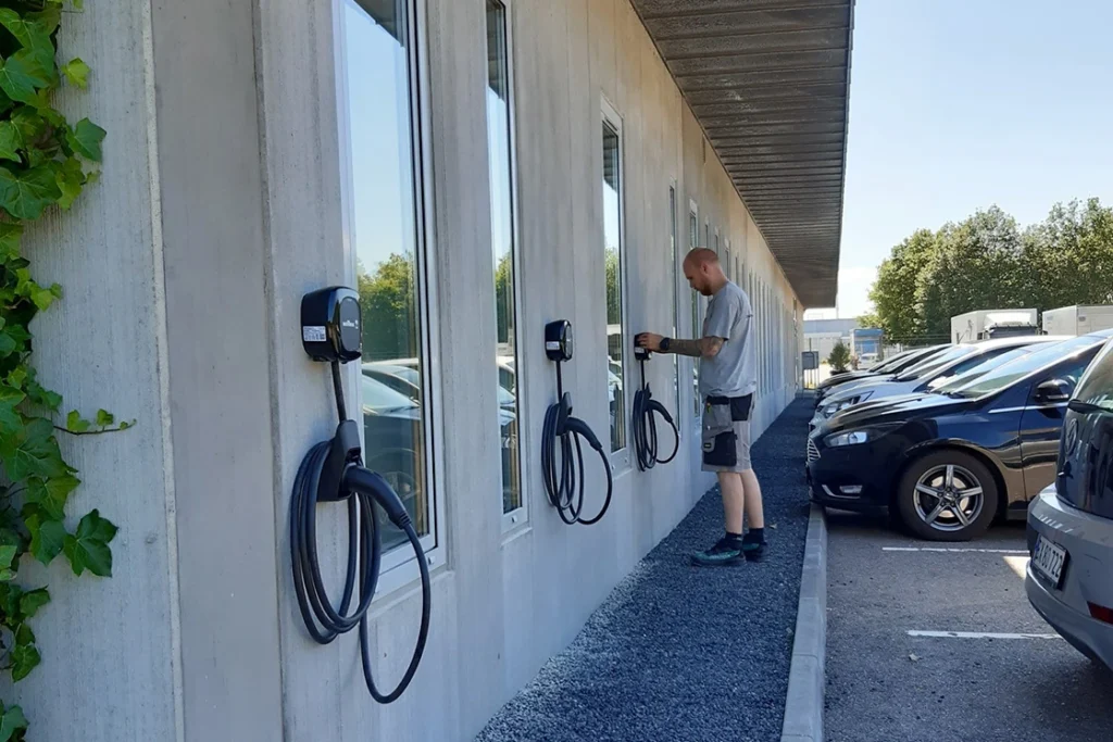 En elektriker fra Uggerly Installation der er ved at montere en ladeboks på væggen af en bolig på en varm sommerdag. 